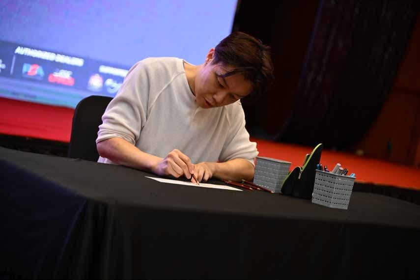 Guest artist seated at a convention signing table sketching on cards with colored pencils